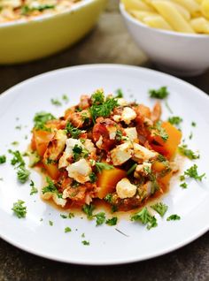 a white plate topped with food next to two bowls filled with pasta and other foods