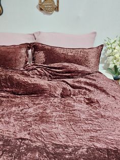 a bed with pink sheets and pillows in a white room next to a vase filled with flowers