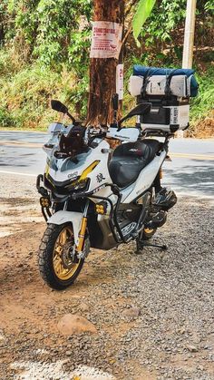 a white motorcycle parked next to a tree on the side of a road near a street sign