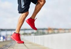 a man in red shoes is running on the edge of a wall with his leg up