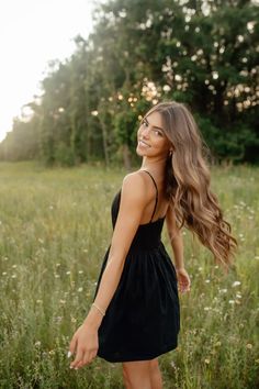a beautiful young woman standing in the middle of a field with her hair blowing in the wind