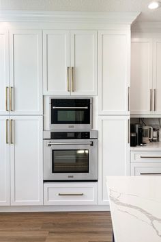 a kitchen with white cabinets and marble counter tops, two ovens are built into the wall