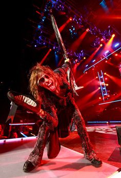 a man dressed as a demon with two swords in his hand on stage at a concert