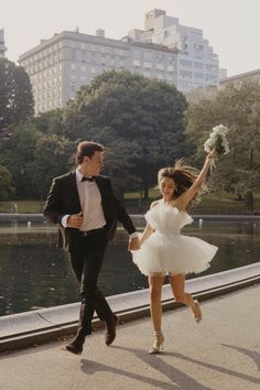 a man in a tuxedo and a woman in a short white dress are holding hands