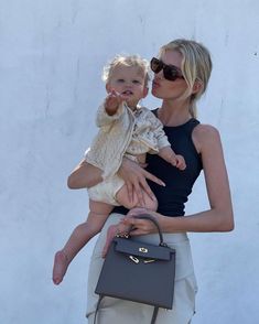 a woman holding a small child in her arms while she holds the baby's purse