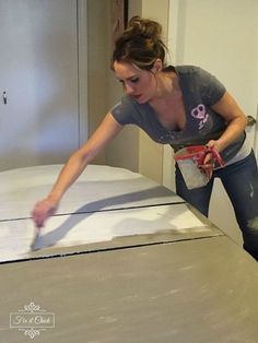 a woman in grey shirt and black pants painting a bed