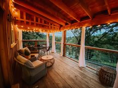 a covered porch with lights strung from the ceiling and furniture on the deck overlooking trees