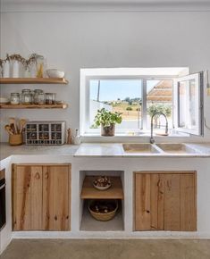 a kitchen with wooden cabinets and open shelves in front of a window that looks out onto the countryside