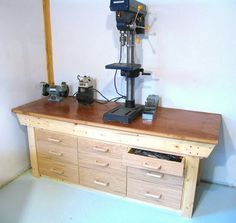 a workbench with two drawers and a driller on the top, in front of a white wall