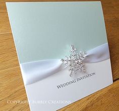 a wedding card with a snowflake on the front and white ribbon around it