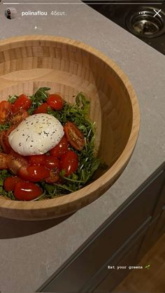 a wooden bowl filled with salad on top of a counter