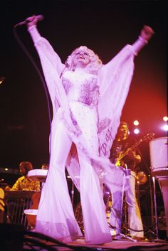 the woman is performing on stage with her arms in the air