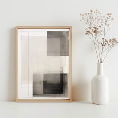 a vase with some flowers in it next to a framed photograph on a wall above a shelf