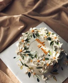 a white cake with flowers on it sitting on a napkin next to a brown cloth