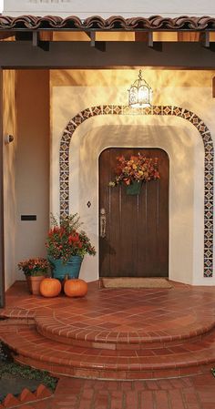 the entrance to a home with potted plants and pumpkins