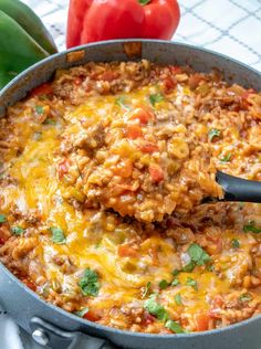 a skillet filled with ground beef and cheese on top of a table next to peppers