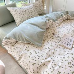 a bed with pillows and a book on it in front of a window, next to a couch