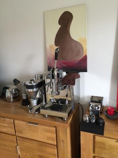 an espresso machine sitting on top of a wooden dresser next to a painting