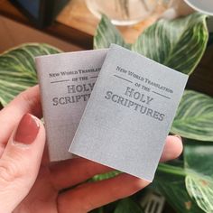 two small book that are held in someone's hand next to some green plants