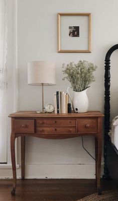 a bed room with a neatly made bed and a wooden table next to it on top of a hard wood floor