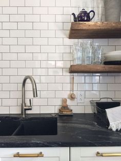 a kitchen with white cabinets and black counter tops, an open shelving above the sink