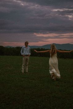 a man and woman standing in the grass with their arms spread out to each other