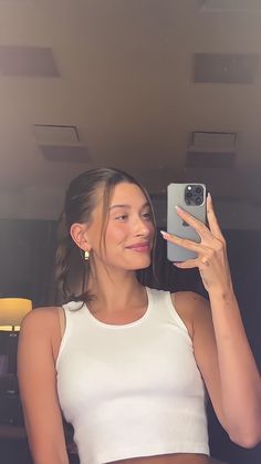 a woman taking a selfie with her cell phone in front of her face and wearing a white crop top