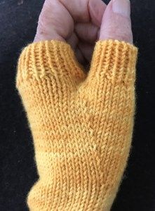 someone is holding their hand up to show the yellow knitted fingerless mitts