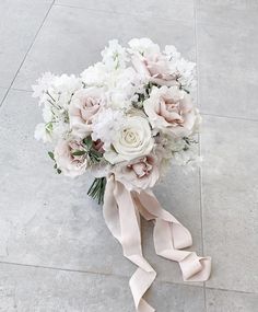 a bouquet of white and pink flowers on the ground with ribbon tied around it's neck