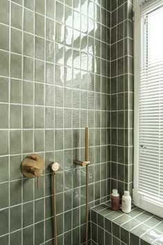 a green tiled bathroom with a window and shower head next to the bathtub in front of it