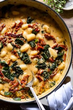 a pot filled with pasta and spinach on top of a wooden table next to silverware