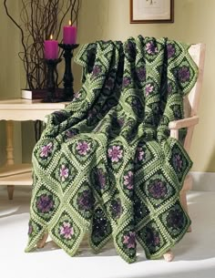 a green crocheted blanket sitting on top of a wooden chair next to a table