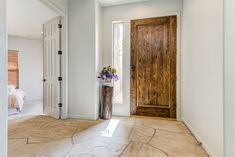 an empty room with a large wooden door and vase on the floor in front of it