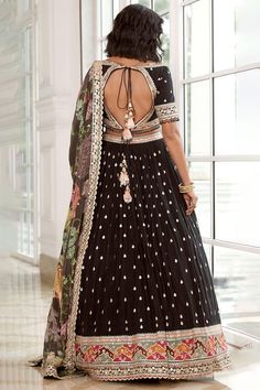 Featured here is a reimagined black georgette lehenga set adorned with bootis and a heavy border showcasing multi-colour thread work both on the lehenga as well as the statement blouse. It is paired with a matching printed floral dupatta with a scalloped border. Style Tip: Finish the look with a kundan polki mala and understated ethnic wedges. Fabric / Material :Georgette Colour: Black Wash Care :Dry Clean Only Please note: Note:- Originally Stitched in 40 & 42 but can alter for size 38 & 40 wit Black Sharara For Reception During Navratri, Black Choli With Intricate Embroidery In Georgette, Floor-length Black Sharara For Eid, Black Floor-length Sharara For Eid, Black Dress With Mirror Work For Navratri, Black Georgette Anarkali Set For Festivals, Black Anarkali Floor-length Sharara, Black Anarkali Style Floor-length Sharara, Black Floor-length Anarkali Sharara