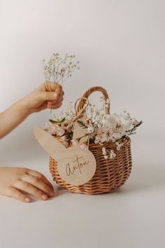 a person holding a basket with flowers in it and a sign that says autumn on it