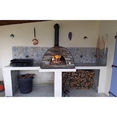 an outdoor pizza oven with logs in the foreground and other items on the wall