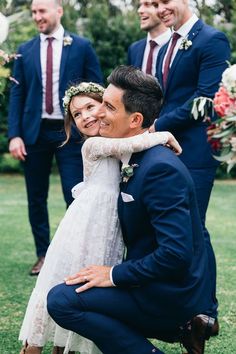 a bride and groom hugging each other in front of their wedding party on the lawn