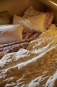 an unmade bed with many pillows and blankets