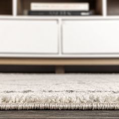 an area rug is on the floor in front of a white entertainment center with bookshelf