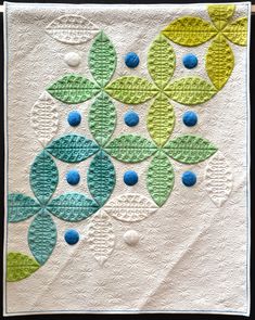 a quilted wall hanging with blue, green and white circles in the shape of leaves