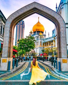 a woman in a yellow dress standing under an arch with a golden dome on top