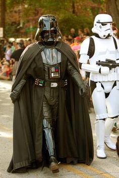 two people dressed as stormtrooper and darth vader walk down the street