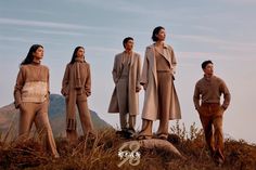 four people standing on top of a hill with their hands in their pockets and looking up at the sky