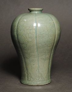 a large green vase sitting on top of a table next to a gray wall and floor