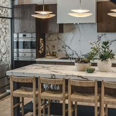 a kitchen with marble counter tops and wooden chairs in front of an island that has potted plants on it