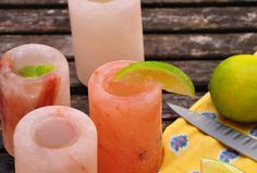 three different types of drinks sitting on a table next to a knife and some lemons