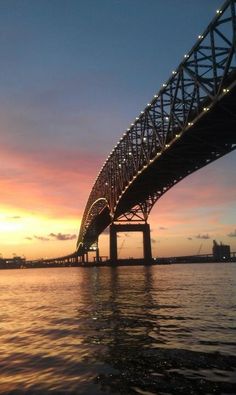 the sun is setting behind a bridge over water