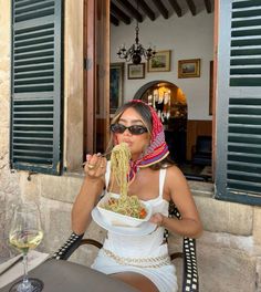 a woman sitting at an outdoor table eating food from a bowl with her hands in her mouth