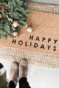 a person standing in front of a door mat that says happy holidays