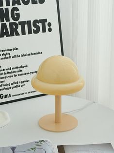 a white table topped with a yellow plastic hat on top of a wooden stand next to a book